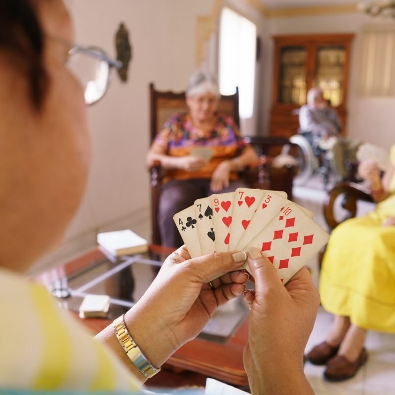Old people in geriatric hospice: group of senior women playing cards and having fun together. The aged ladies sit on the sofa of the hospital and start a new match